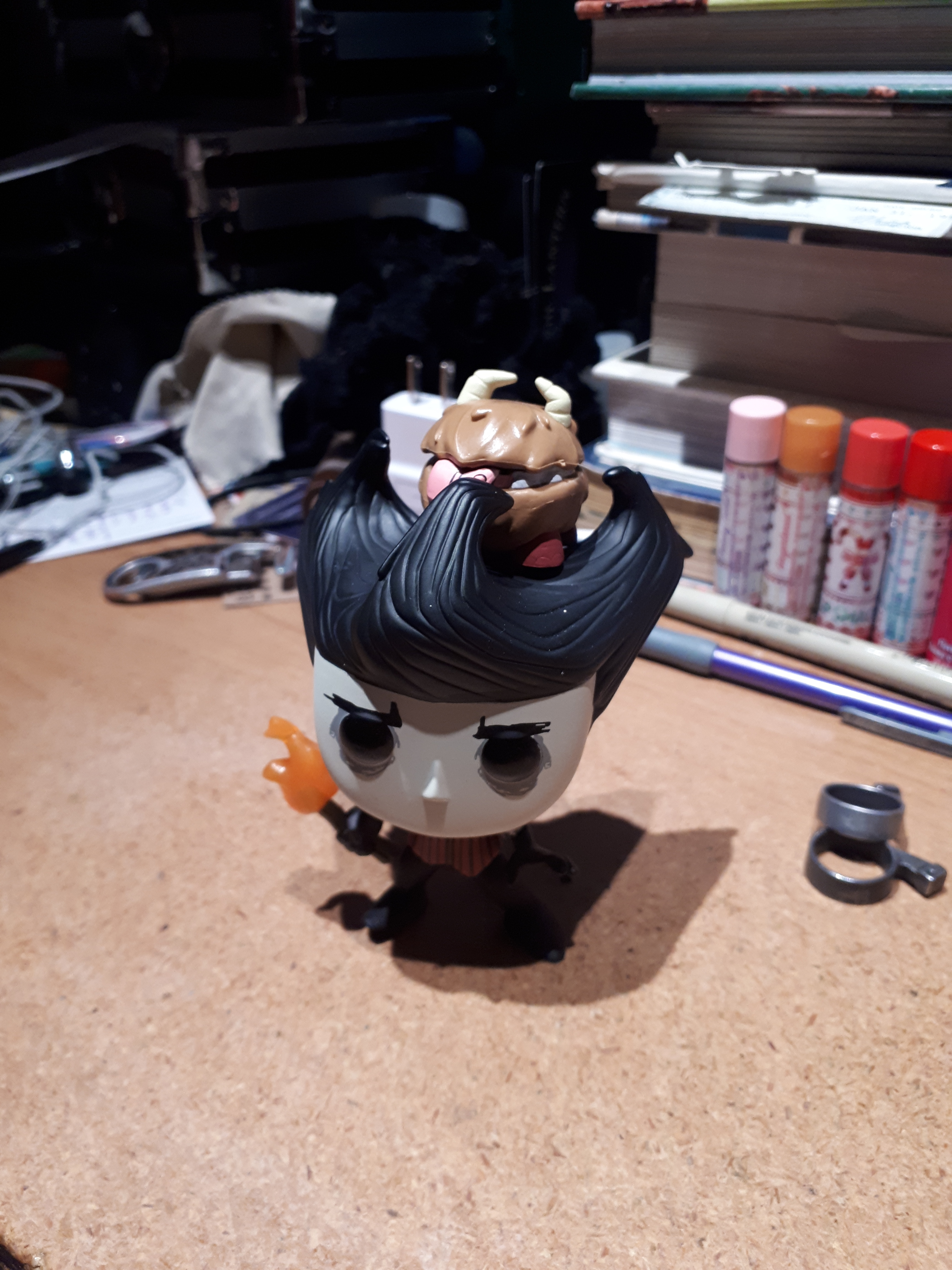 A Wilson Funko Pop standing on my mildly cluttered desk, with the included Chester sitting between the hair prongs on his head.