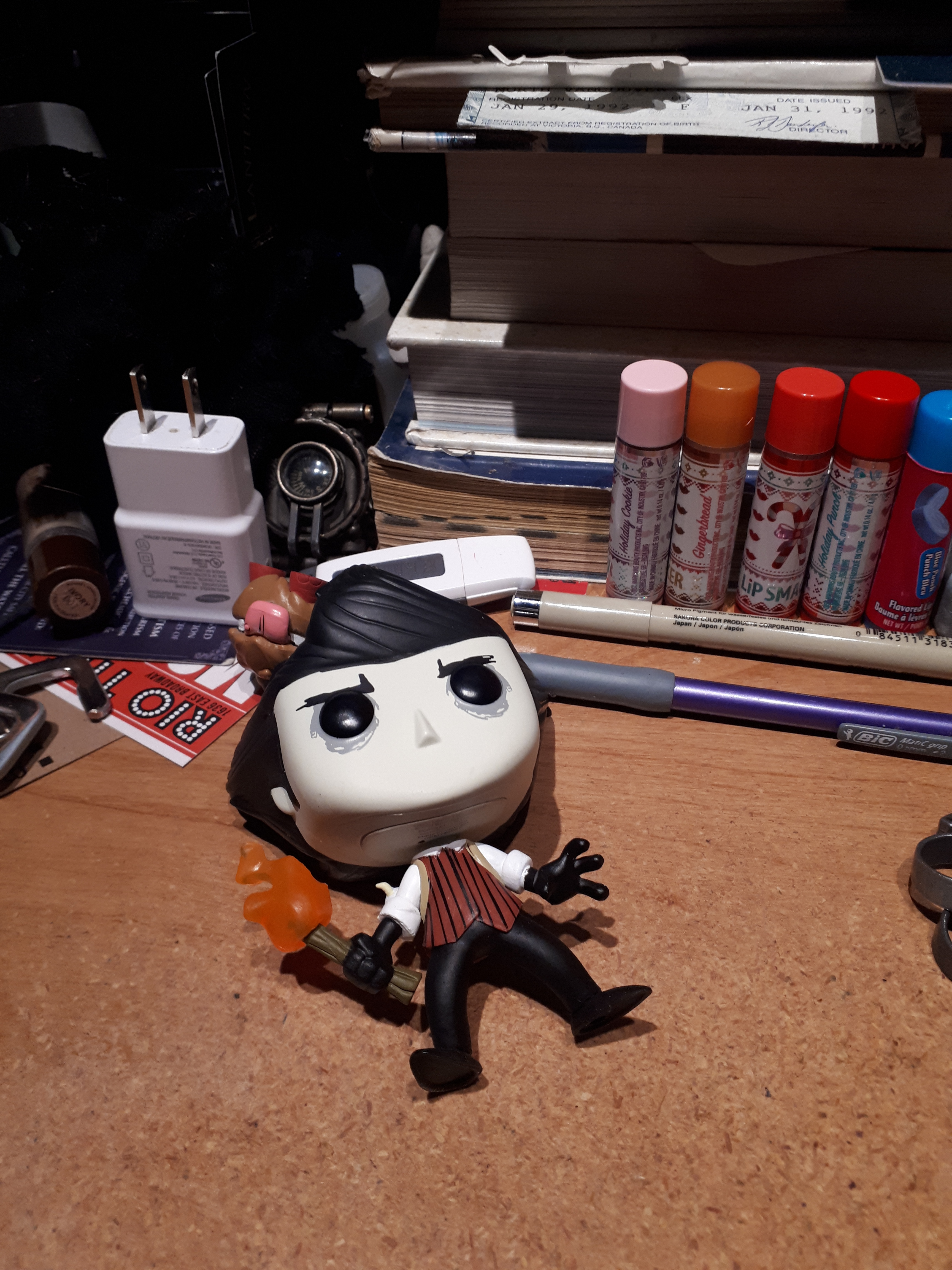 A Wilson Funko Pop flat on his back on my desk, with Chester upended behind him.